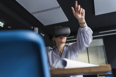 Young woman wearing VR glasses at table in office - UUF12844