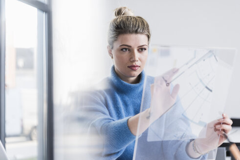 Junge Frau arbeitet an einem transparenten Entwurf im Büro - UUF12851