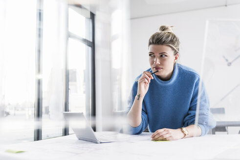 Junge Frau mit Laptop am Schreibtisch im Büro denkt nach - UUF12853