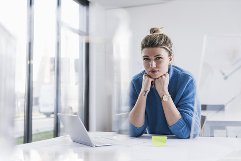 Portrait of young woman with laptop at desk in office stock photo