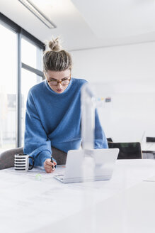 Junge Frau mit Laptop und Plan bei der Arbeit am Schreibtisch im Büro - UUF12858