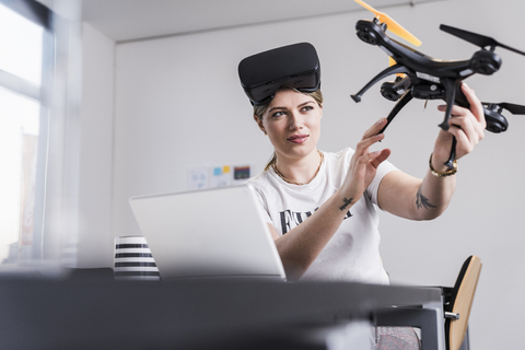 Young woman with laptop and VR glasses at desk holding drone stock photo