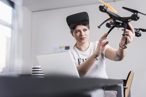 Junge Frau mit Laptop und VR-Brille am Schreibtisch mit Drohne - UUF12863