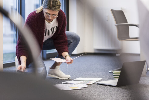 Junge Frau mit Laptop und Dokumenten bei der Arbeit auf dem Boden im Büro - UUF12866