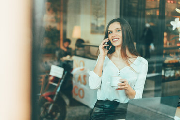 Porträt einer glücklichen jungen Frau beim Telefonieren in einem Café - OCAF00162