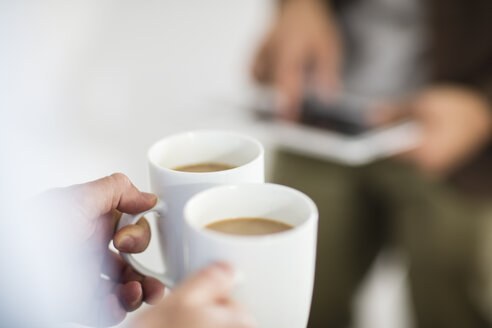 Nahaufnahme einer Frau, die eine Kaffeetasse hält, während ein Mann ein Tablet im Büro benutzt - ZEF15033