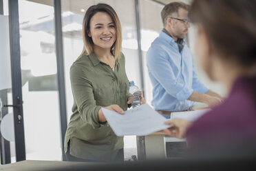 Lächelnde Geschäftsfrau im Büro, die einem Kollegen Papier übergibt - ZEF15050