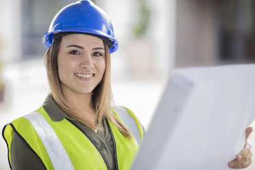 Portrait of smiling woman wearing hard hat and reflective jacket holding plan - ZEF15056