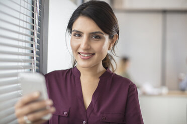 Porträt einer lächelnden Geschäftsfrau, die ein Mobiltelefon im Büro hält - ZEF15058
