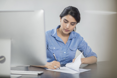 Geschäftsfrau macht sich Notizen am Schreibtisch im Büro, lizenzfreies Stockfoto
