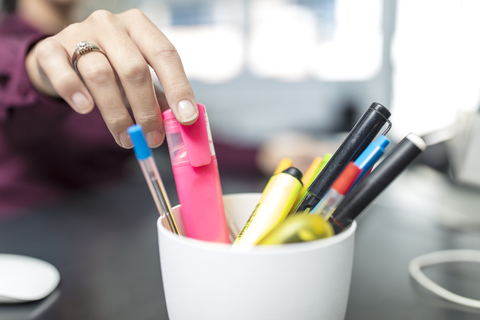 Frau am Schreibtisch im Büro nimmt Textmarker aus Stifthalter, lizenzfreies Stockfoto