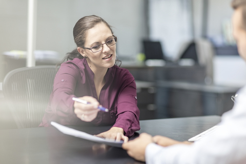 Frau zeigt einem Kunden am Schreibtisch den Vertrag, lizenzfreies Stockfoto