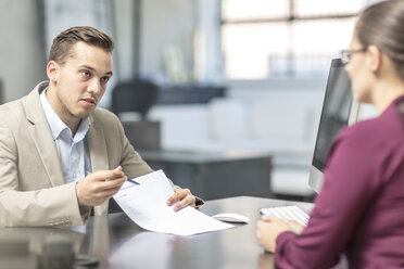 Man showing document to woman at desk - ZEF15084