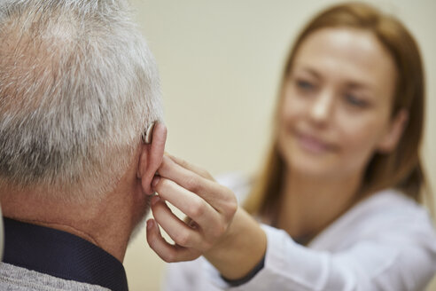 Female doctor applying hearing aid to senior man's ear - ZEDF01253