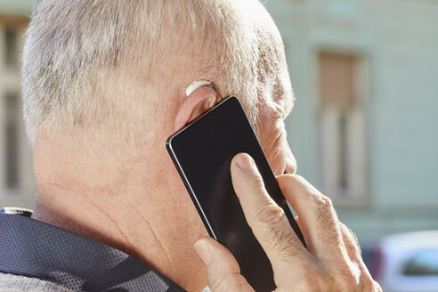 Close-up of senior man with hearing aid using smartphone - ZEDF01256
