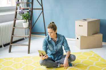 Woman sitting on floor of her new apartment, using digital tablet - MOEF00866