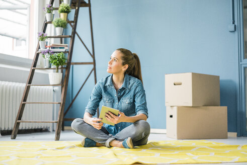 Woman sitting on floor of her new apartment, using digital tablet - MOEF00868