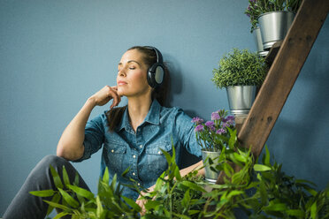 Schöne Frau in ihrem Haus, dekoriert mit Pflanzen, hört Musik mit Kopfhörern - MOEF00879