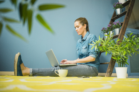 Schöne Frau in ihrem Haus, dekoriert mit Pflanzen, mit Laptop, lizenzfreies Stockfoto