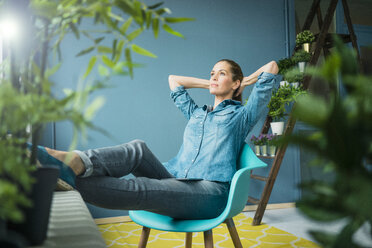 Beautiful woman sitting in her home, decorated with plants, daydreaming - MOEF00887