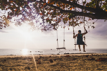 Thailand, Phi Phi Inseln, Ko Phi Phi, Mann auf Baumschaukel am Strand bei Sonnenuntergang - KKAF00891