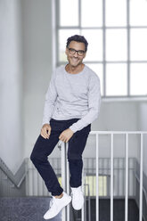 Portrait of smiling man sitting on railing of staircase - PNEF00549