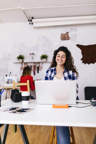 Lächelnde Modedesignerin mit Laptop im Atelier, lizenzfreies Stockfoto