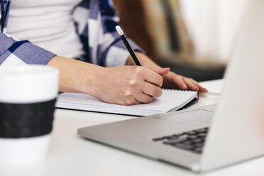 Close-up of woman with laptop taking notes at desk - JRFF01566