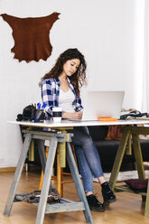 Fashion designer with laptop taking notes in studio - JRFF01570
