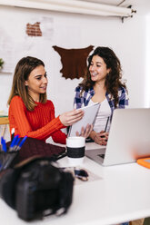 Two fashion designers working in studio with laptop and notebook - JRFF01583