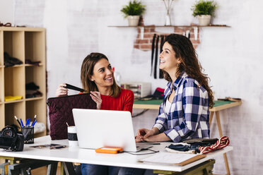 Zwei lächelnde Modedesigner arbeiten im Atelier mit Laptop - JRFF01584