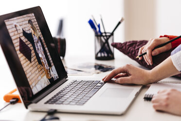 Nahaufnahme von zwei Modedesignern bei der Arbeit an einem Foto auf einem Laptop - JRFF01585