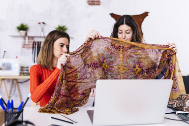 Two fashion designers in studio with laptop examining fabric - JRFF01588