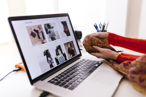 Nahaufnahme eines Modedesigners im Studio mit Laptop, der Stoffe untersucht, lizenzfreies Stockfoto