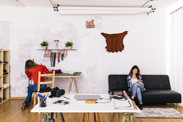 Two women in fashion studio using sewing machine and cell phone - JRFF01593