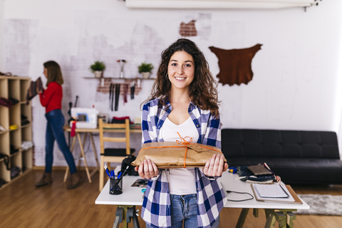 Lächelnde Modedesignerin hält ein eingepacktes Paket im Atelier, lizenzfreies Stockfoto