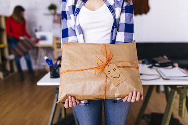 Nahaufnahme eines Modedesigners, der ein verpacktes Paket in einem Atelier mit einem Smiley hält - JRFF01604