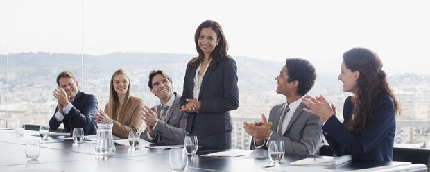 Co-workers clapping for businesswoman in conference room - CAIF00015