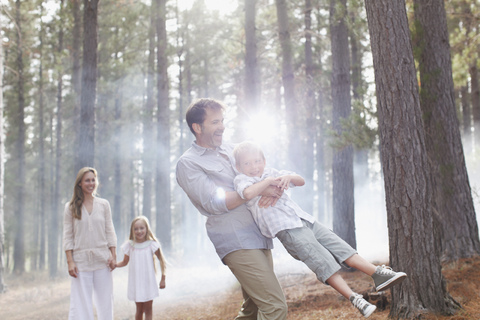 Glückliche Familie beim Spielen im sonnigen Wald, lizenzfreies Stockfoto