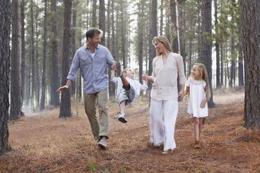 Happy family holding hands and walking in woods - CAIF00056