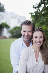 Porträt eines lächelnden Paares im Hof mit Haus im Hintergrund - CAIF00060