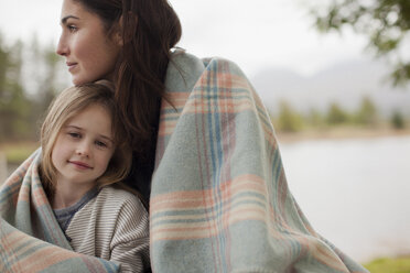 Portrait of smiling daughter wrapped in blanket with mother at lakeside - CAIF00078