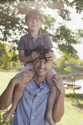 Vater trägt lächelnden Sohn auf den Schultern am Seeufer - CAIF00083