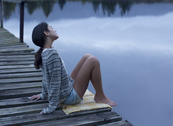 Serene woman sitting on dock over lake - CAIF00084