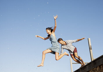 Exuberant couple jumping off dock - CAIF00087