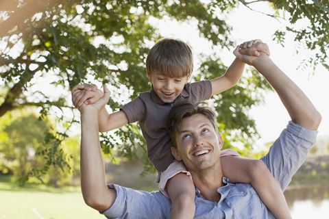 Lächelnder Vater trägt seinen Sohn auf den Schultern unter einem Baum, lizenzfreies Stockfoto