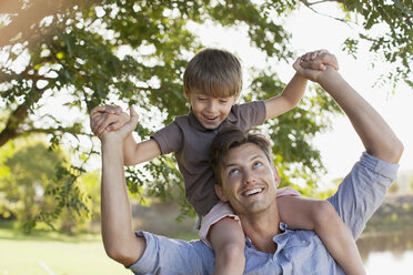 Lächelnder Vater trägt seinen Sohn auf den Schultern unter einem Baum - CAIF00109
