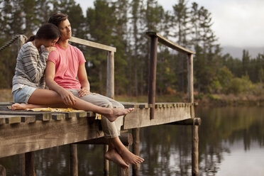 Serene couple sitting at edge of dock over lake - CAIF00122