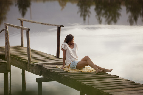 Frau sitzt auf dem Steg über dem See, lizenzfreies Stockfoto