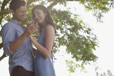 Smiling couple holding hands under tree - CAIF00132